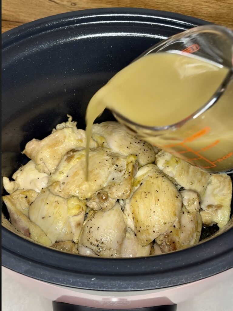 mojo criollo being poured over chicken thighs in a slow cooker